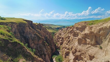 Obraz premium High above, a wide view of a canyon cutting through the land. Issyk Kul Lake is in sight. The scene shows rough, worn hills in Kyrgyzstan, Asia. 