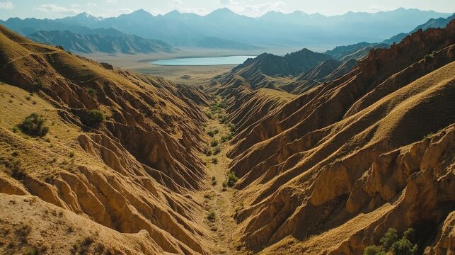 High above, a wide view of a canyon cutting through the land. Issyk Kul Lake is in sight. The scene shows rough, worn hills in Kyrgyzstan, Asia.
