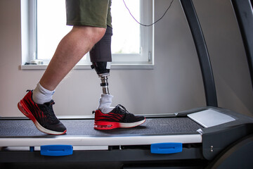 Man with prosthetic leg on treadmill in gym. Amputation and use of an artificial leg. Training exercises to maintain health. Person with amputation.