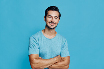 Smiling man with crossed arms wearing a casual blue t-shirt stands against a solid turquoise...