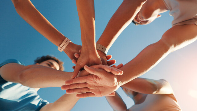 People, team and hands together in fitness with blue sky below for motivation, unity or mission. Low angle, group or friends piling with stack in huddle, circle or solidarity for health and wellness