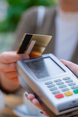 Close-up person making a contactless payment using a credit card on a POS terminal. The scene takes place in a cafe setting with a teapot in the background, showing modern transaction ease .Vertical