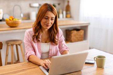 Beautiful woman freelancer noting information for planning project doing remote job via laptop computer. woman laughing while reading email on modern laptop device .