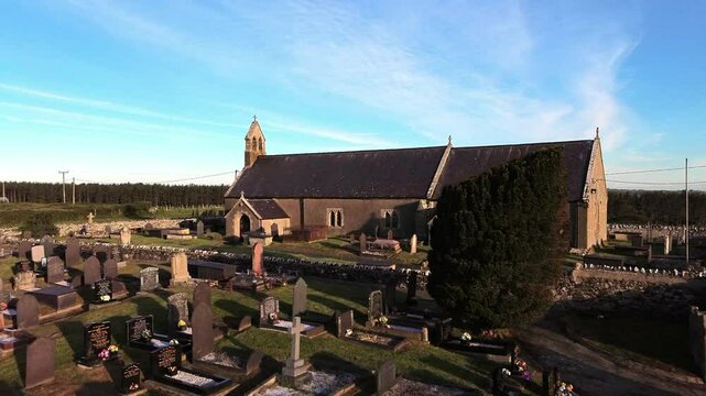 St Peters church in rural Newborough aerial view rising across Welsh slate gravestones at sunrise