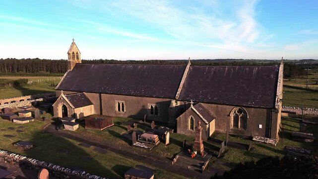 St Peters church in rural Newborough aerial orbit view across Welsh slate gravestones at sunrise