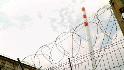 Barbed wire protecting industrial chimney emitting smoke into cloudy sky