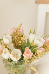 Elegant bouquet of white and pink tulips with yellow mimosa flowers in an interior setting. Fresh spring bloom for holiday celebration.