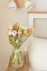 Bouquet of tulips and mimosa flowers in a vase on a bedside table. Interior decoration with fresh flowers in a home setting.