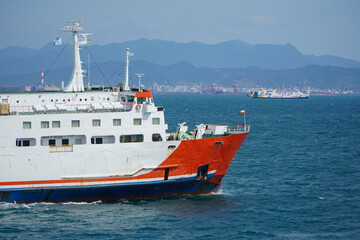 Cargo Ship Navigating Calm Waters with Mountains in the Background Near a Coastal Harbor