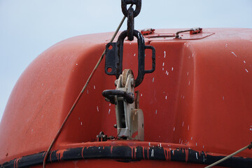 Close-up of an Orange Life Boat Hook and Hang Mechanism Suspended in a Marine Setting