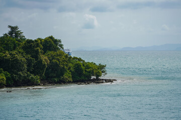 Naklejka premium Coastal Landscape Featuring Lush Green Island and Calm Waters Under a Cloudy Sky