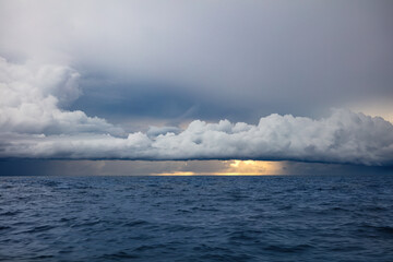 Storm clouds off the coast of Northern Bali, Indonesia. Rain pouring from clouds into the ocean. Blue sea in the foreground. 
