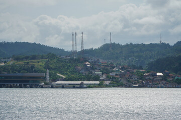 Distant View of a Coastal City and Hills Reflected in Calm Waters Under Cloudy Sky