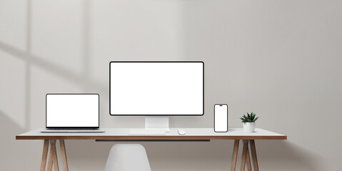 Fototapeta premium Bright office desk with laptop, computer monitor, and smartphone mockups, blank wall space for promotional copy