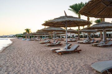 Relaxation on a quiet beach with thatched umbrellas and sun loungers at sunset in a tropical paradise