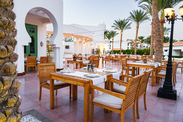 Outdoor dining area in a tropical restaurant with palm trees and elegant furnishings during sunset