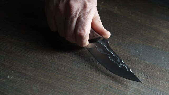 Man's hand takes a forged sharp knife from the wooden table, close up. Iron knife with shiny blade  in male hands