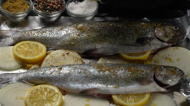 The chef pours fresh lemon juice on the two prepared trout fish carcasses for baking in the oven on a baking sheet, close up