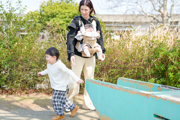 In spring at a park in Fukuoka, a mom in her thirties poses with her 3-year-old son and 6-month-old baby girl. They look at the camera. This photo captures a calm and loving family moment in nature.