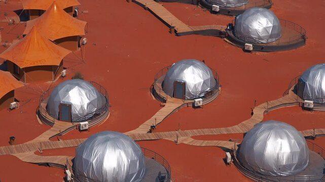 Elevated view of geodesic domes and tents resembling a Mars colony base on a red desert landscape. This unique structure serves as futuristic accommodation.
