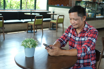 An elderly Asian man in a red plaid shirt happily uses his phone for the first time in a coffee shop.