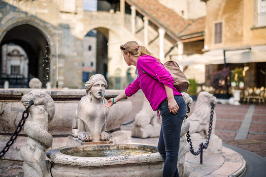 Fototapeta Tourist woman standing at Contarini fountain statue in Piazza Vecchia old town of Bergamo, Italy, enjoying cultural summer holiday
