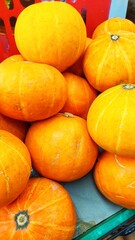 This is a close-up shot of a pile of bright orange, round squashes, likely kabocha or a similar variety. They are varying slightly in size, and some have remnants of a stem at the top. 
