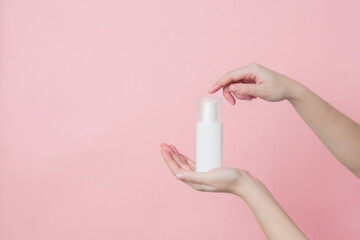 White unbranded cream bottle with pump in hand on pink background. Concept of beauty. Product cosmetic advertising