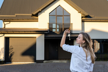 Happy woman standing with house keys in front of residential home. Property lease real estate for relocation. Leasing insurance and purchase.