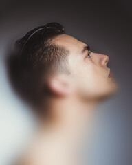 Conceptual collage. Young man in profile lit from below, eyes turned upward in soft gradient, expressing hope and concentration. Concept of strength, thought, light, male identity, inner peace.