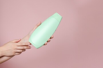 Elegant hand with shampoo light bottle isolated on solid pink background. Package for cosmetics product, your brand, spa, beauty. Space for text