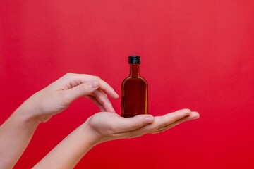 Elegant hand with small glass blank bottle mockup on red background. Package for cosmetics product, nutritional supplements, mixture, alcohol. Space for text