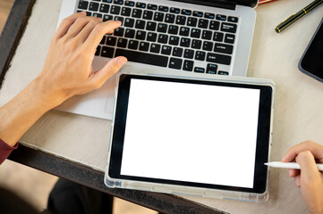 Close up of hand with stylus pointing at white screen tablet on laptop while sitting at table.
