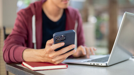Close up of a hand holding smartphone with another hand touching on laptop while sitting at table