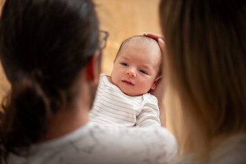 Tender moment as parents lovingly cradle their newborn, capturing the warmth and bond of family. The baby, dressed in a striped outfit, gazes upward, conveying innocence and peace