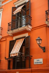 Bright Orange Building Exterior with Balconies and Striped Awnings, Italy