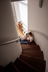 Young parents sitting on stairs at home, cuddling and kissing their baby, cherishing precious moments together while enjoying the warmth of family love and togetherness