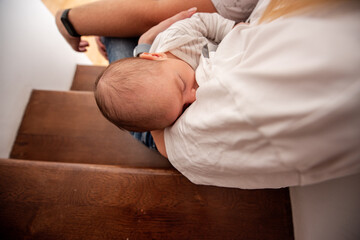 Young mother sitting on wooden stairs breastfeeding her newborn baby, enjoying a peaceful moment of bonding and nourishment in the comfort of their home