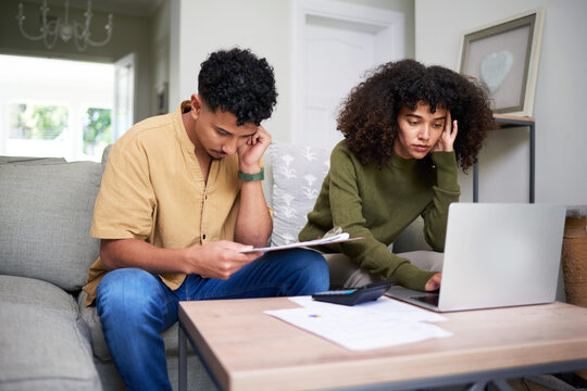 Focused Couple Reviewing Financial Documents and Using a Laptop Together at Home