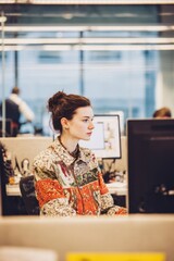 In an open office with large desks and computers A worker in fusion attire, a modern jacket with traditional fabric patterns, checks emails The mood is calm and efficient