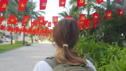 Woman walking through lively hanoi street, red national flags waving, capturing festive independence day atmosphere during bright summer midday