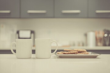 In a clean office kitchenette during a quick break Tea cups are placed on the counter next to a tray of cookies The mood is relaxed and simple