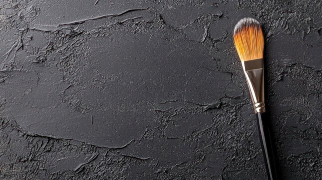 Close-up of a makeup brush with a black handle and orange bristles. the brush is resting on a dark, textured surface with cracks and crevices.