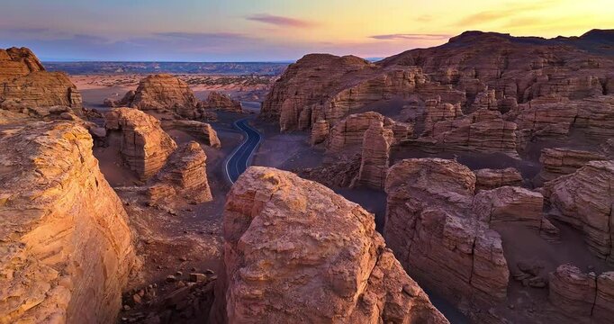 Aerial shot of a winding asphalt road through yardang landform mountain at sunset in Xinjiang, China.