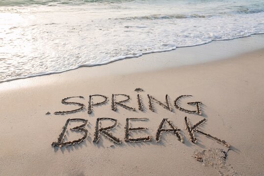 Spring Break Written In Sand On Sunny Beach With Ocean Waves And Footprint