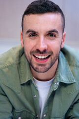 Fototapeta premium Vertical Portrait of a confident young caucasian man smiling at the camera in a stylish and bright kitchen interior, suggesting a relaxed and welcoming home atmosphere with visible food and cooking