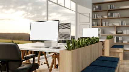 Blank screen computers on table with armchairs near partition bench in office with wide glass wall.