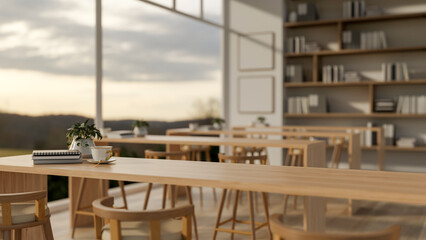 Coffee cup and book on wooden counter or long table on parquet floor in dining hall with glass wall.