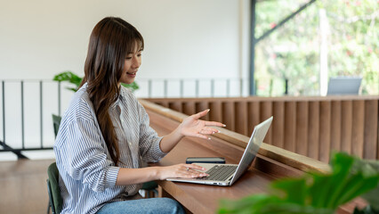 Woman explaining to online meeting or a class on laptop sitting at wooden counter in cafe or library