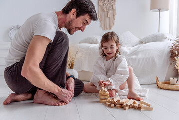 Dad and his little daughter sitting on the floor, playing joyfully with colorful wooden blocks, sharing laughter and creating cherished memories in their cozy bedroom
